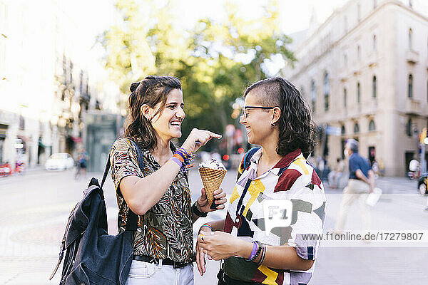Lesbian daubing ice cream on girlfriend's nose while standing in city