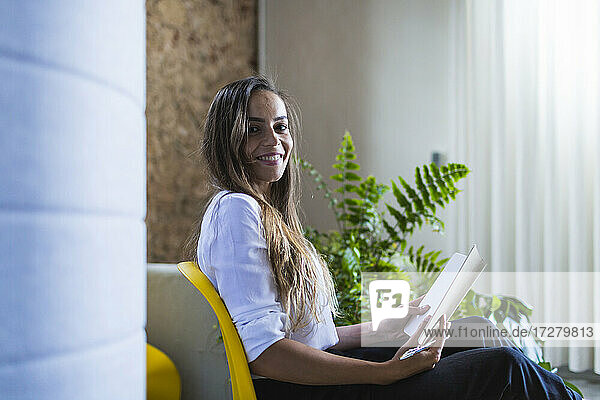 Lächelnde Geschäftsfrau mit Tagebuch auf einem Stuhl im Büro sitzend