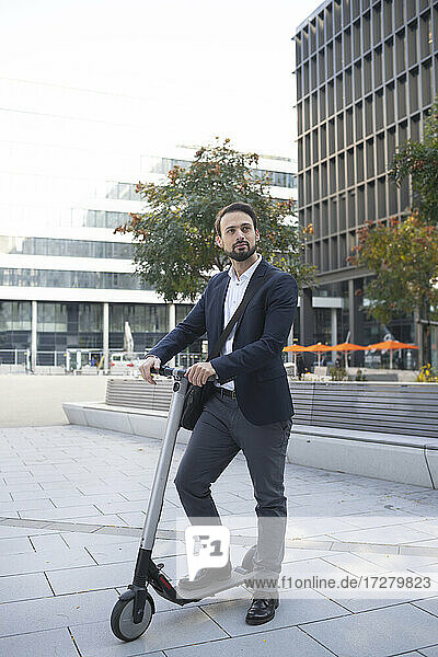 Male business person with electric scooter against building in city