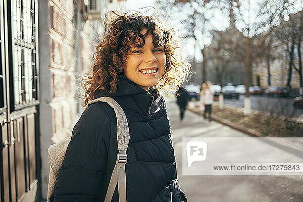 Frau mit Tasche,  die lächelnd auf dem Bürgersteig in der Stadt steht