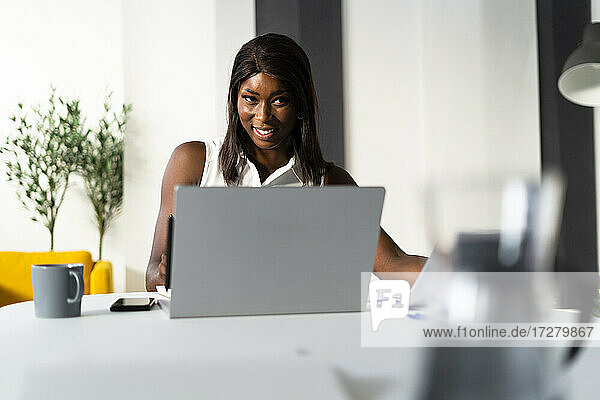 Smiling businesswoman working on laptop while sitting by desk at office