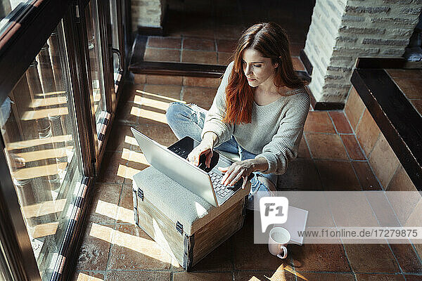 Frau arbeitet am Laptop  während sie zu Hause auf dem Boden sitzt