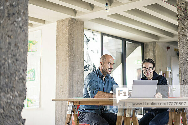 Lächelnder Geschäftsmann und Frau mit Laptop bei der Arbeit im Büro