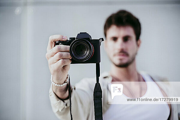 Man taking photograph through camera while standing against wall
