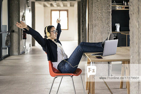 Carefree woman with arms outstretched sitting with legs on table at office
