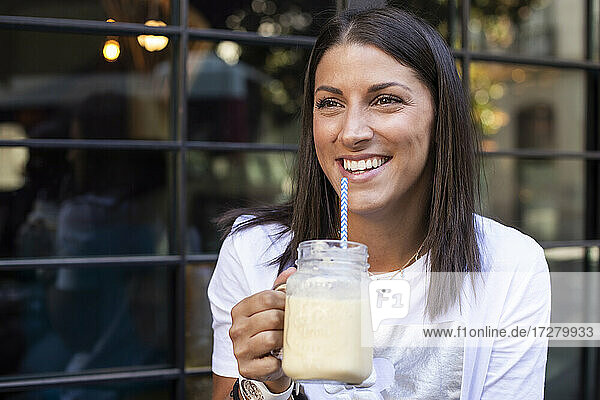 Fröhliche junge Frau genießt ein Getränk aus einem Einmachglas an einer modernen Bar und schaut sich um