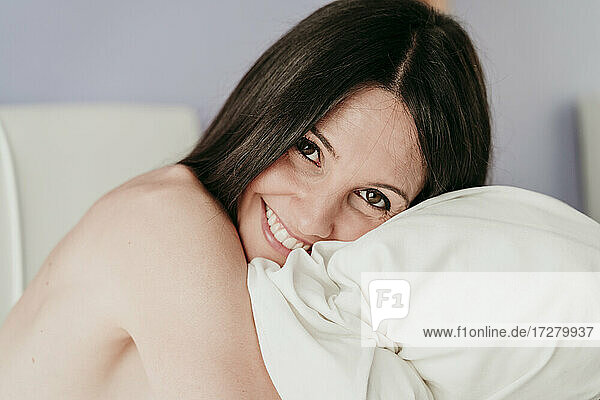 Lächelnde schöne Frau umarmt Decke im Schlafzimmer zu Hause