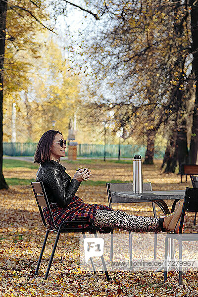 Mittlere erwachsene Frau trinkt Kaffee  während sie in einem öffentlichen Park sitzt