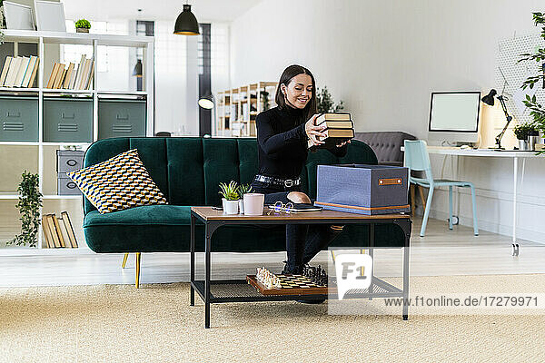 Smiling beautiful woman collecting books in box on coffee table at loft apartment