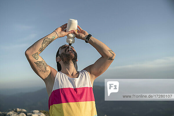 Athlete drinking water while standing on mountain against clear sky