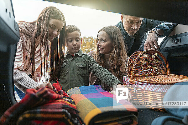 Family picking up picnic stuff from car trunk