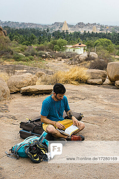 Junger Mann liest ein Buch  während er auf dem Boden sitzt  Karnataka  Hampi  Indien