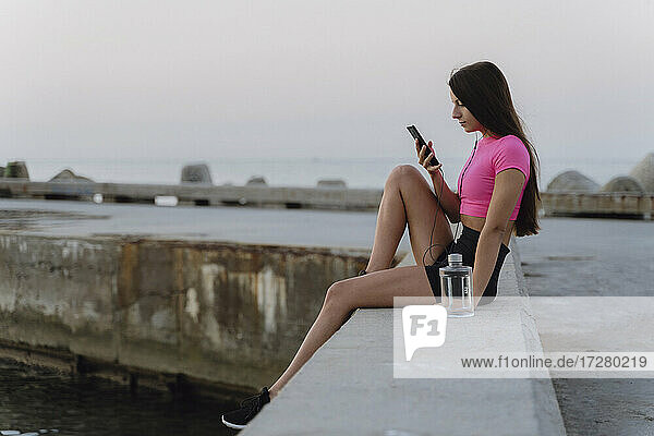 Woman using mobile phone while sitting on retaining wall