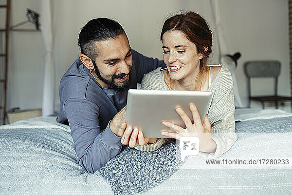 Smiling couple using digital tablet while lying on bed at home