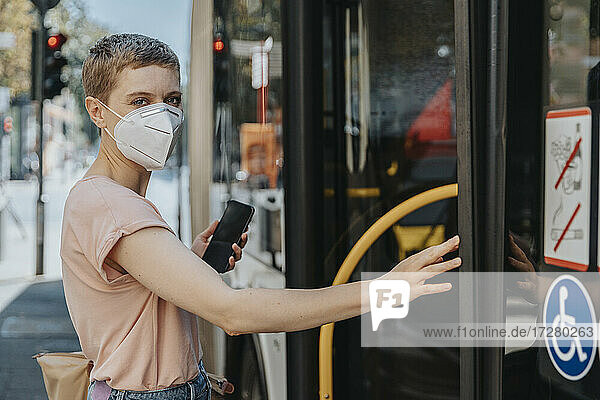 Frau mit Gesichtsschutzmaske beim Einsteigen in den Bus auf der Straße in der Stadt