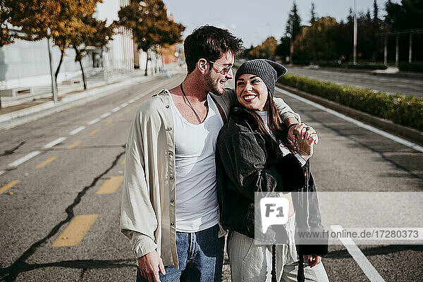 Smiling woman holding hands with male partner while standing on road in city