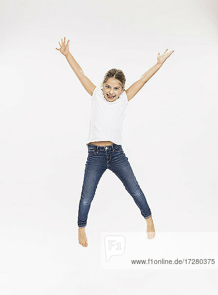 Kleines Mädchen springt mit erhobenen Armen vor weißem Hintergrund im Studio