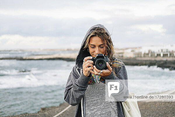 Junge Frau  die am Strand stehend mit der Kamera fotografiert
