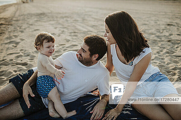 Husband and wife spending time with son at beach during sunset