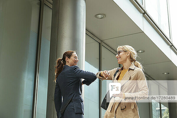 Geschäftsfrau und Kollege grüßen sich mit Ellbogenstoß  während sie in der Stadt stehen