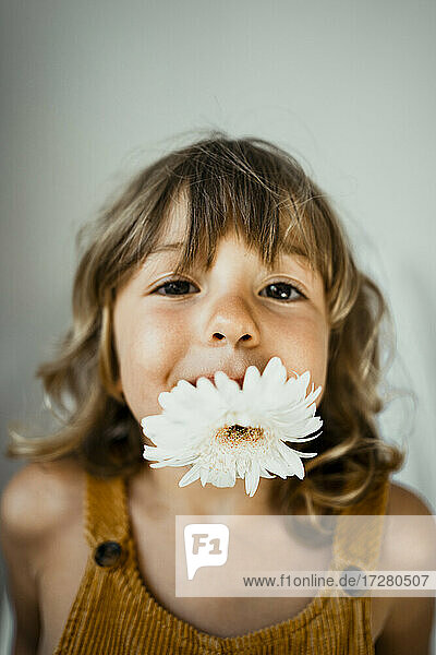 Niedliches Mädchen mit Blume im Mund an der Hauswand