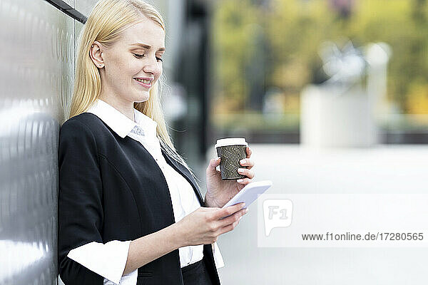 Blond businesswoman drinking coffee while leaning on wall