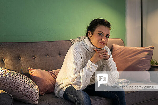 Smiling woman with hand on chin sitting on couch at home