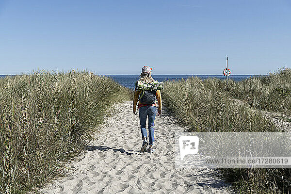 Rückansicht einer Frau mit Rucksack  die am Strand spazieren geht