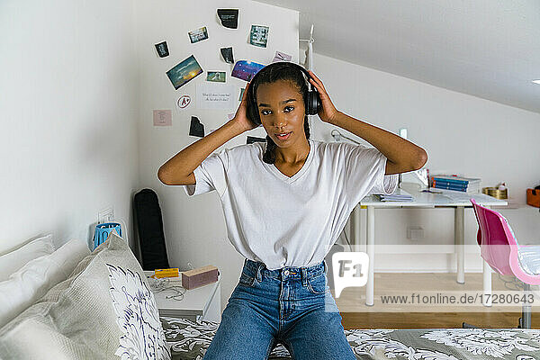 Teenager-Mädchen kniet auf dem Bett und hört Musik über Kopfhörer zu Hause
