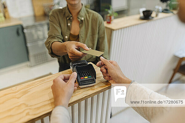 Mittelteil einer Unternehmerin  die einem Kunden an der Kasse eines Cafés eine Kreditkarte gibt