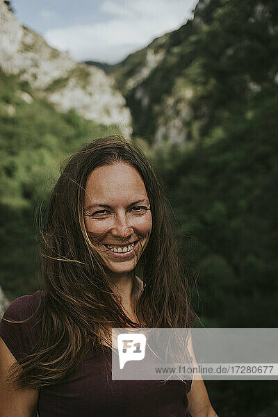 Lächelnde mittelgroße erwachsene Frau mit langen braunen Haaren vor einem Berg