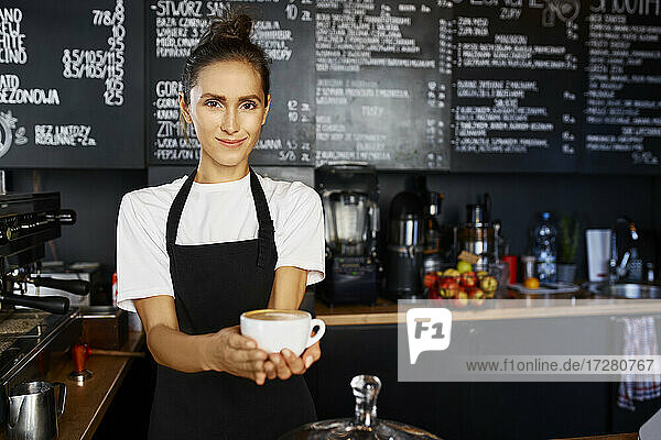 Porträt einer lächelnden Kellnerin  die in einem Café Kaffee ausschenkt
