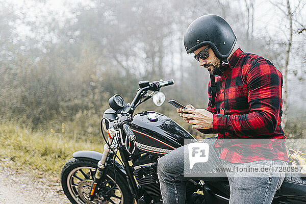 Mann benutzt sein Smartphone auf dem Motorrad sitzend während einer Autofahrt