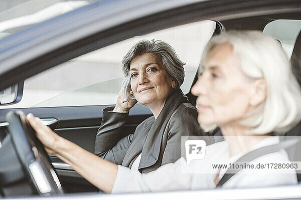 Geschäftsfrau lächelt  während sie neben einer Kollegin sitzt  die in der Stadt Auto fährt