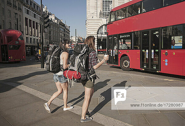 Female friends with backpacks walking in city on sunny day