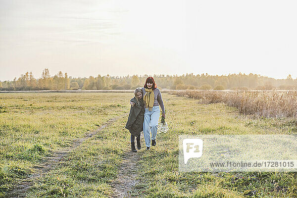 Senior woman walking with granddaughter on field during sunny day