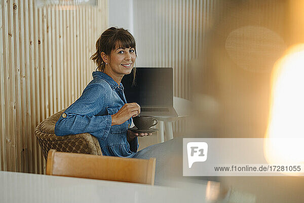 Lächelnde Besitzerin mit Kaffeetasse an einer Holzwand in einem Café