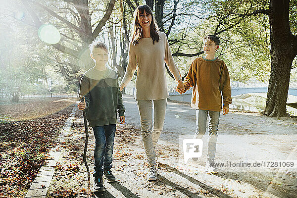 Happy mother and sons walking in public park on sunny day