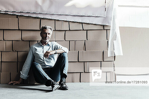 Thoughtful businessman sitting against boxes in factory