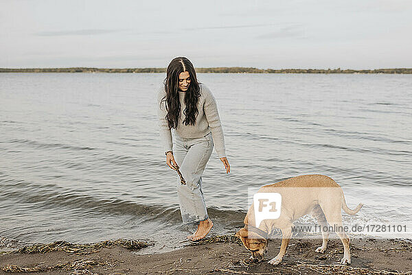 Frau spielt mit Hund  während sie bei Sonnenuntergang im See steht