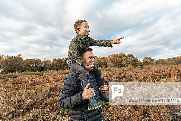 Vater  der seinen Sohn auf der Schulter trägt  steht im Herbst im Park von Cannock Chase vor einem bewölkten Himmel