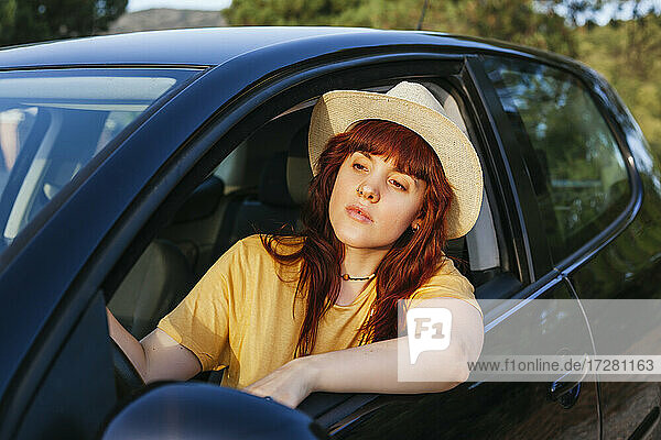 Young redhead woman leaning out from car window during road trip