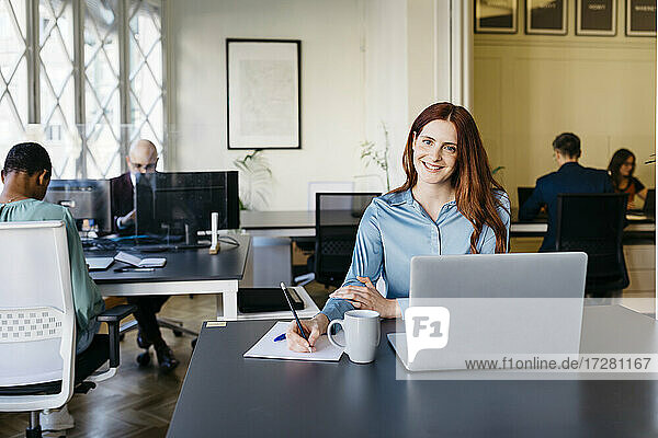 Smiling businesswoman writing in paper at office desk