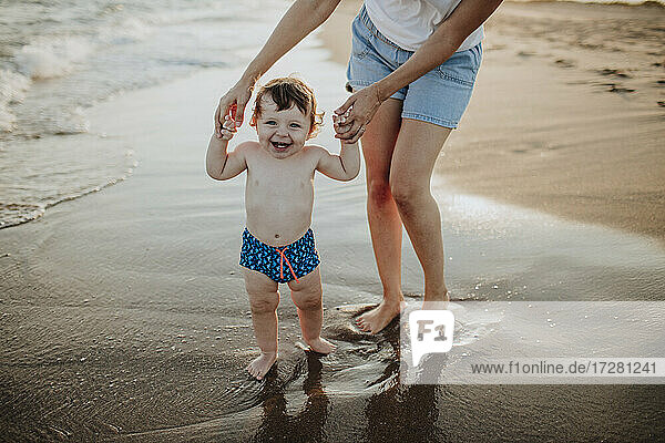 Mittelteil der Mutter mit lächelndem Sohn am Strand bei Sonnenuntergang