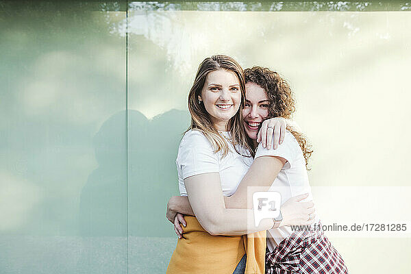 Smiling beautiful women hugging each other against wall
