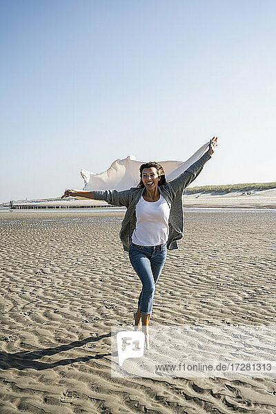Fröhliche Frau  die am Wochenende am Strand läuft und eine Decke hält