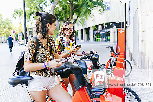 Freundinnen benutzen ein Handy  während sie an einer Fahrradabstellanlage stehen