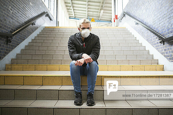 Jugendliches Mädchen mit Schutzmaske und Handschuhen auf der Treppe eines Bahnhofs sitzend