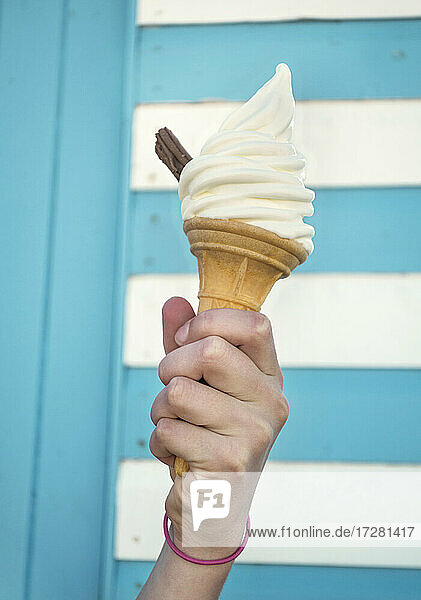 Close-up of girl's hand holding ice cream cone against striped wall