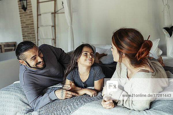 Eltern und Tochter im Gespräch auf dem Bett liegend zu Hause